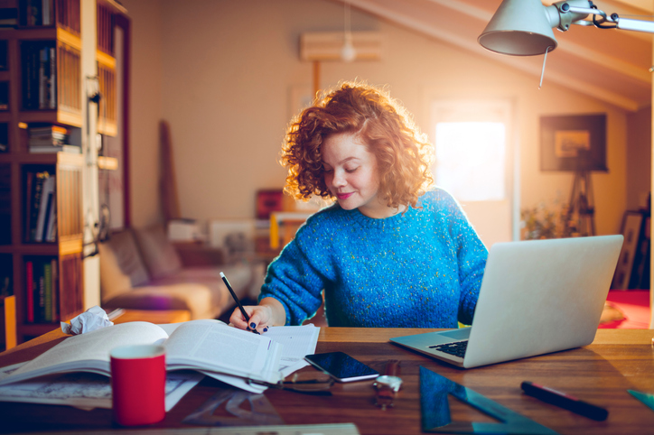 Young woman studying at her desk while working on a laptop