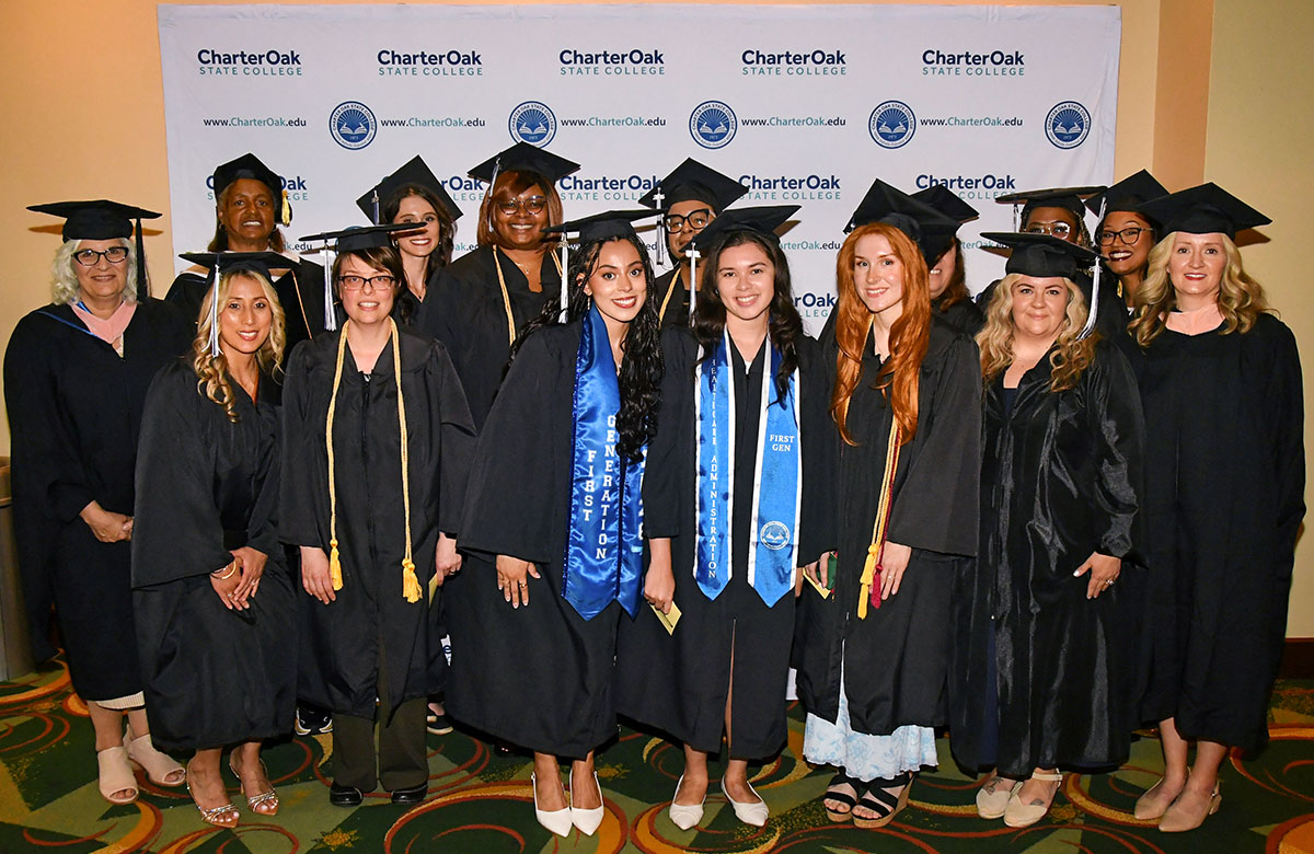 Charter Oak graduate in cap and gown in front of the college's branded backdrop