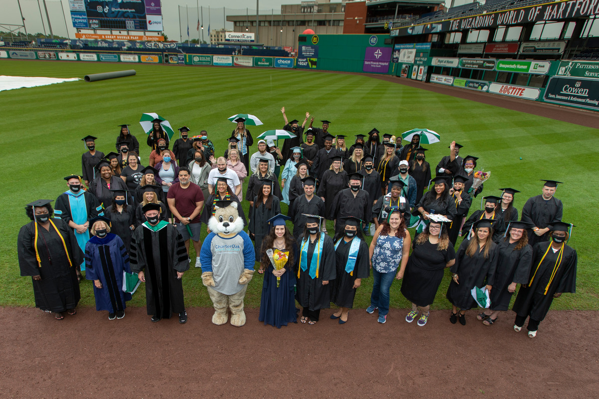 Graduation Celebration at yard goats stadium with oaklee the charter oak mascot, graduates in cap and gown on the baseball field, with faculty and administrators too 2021