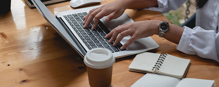 Person typing on a laptop on a desk with coffee and notepad