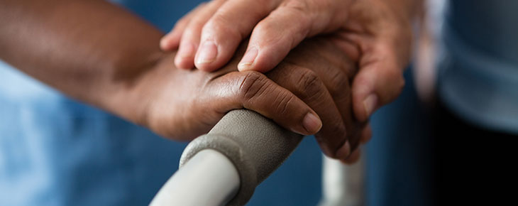 Hands of nurse and woman holding walker in nursing home