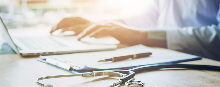 Health care professional typing information on laptop in hospital office focus on stethoscope