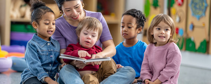 Teacher sitting on the floor with young children reading.