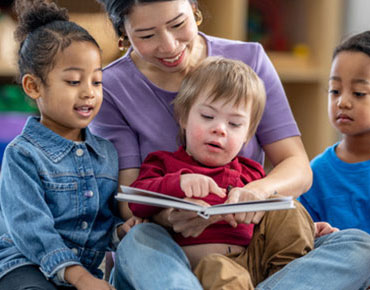 Teacher reading a book with children on her lap